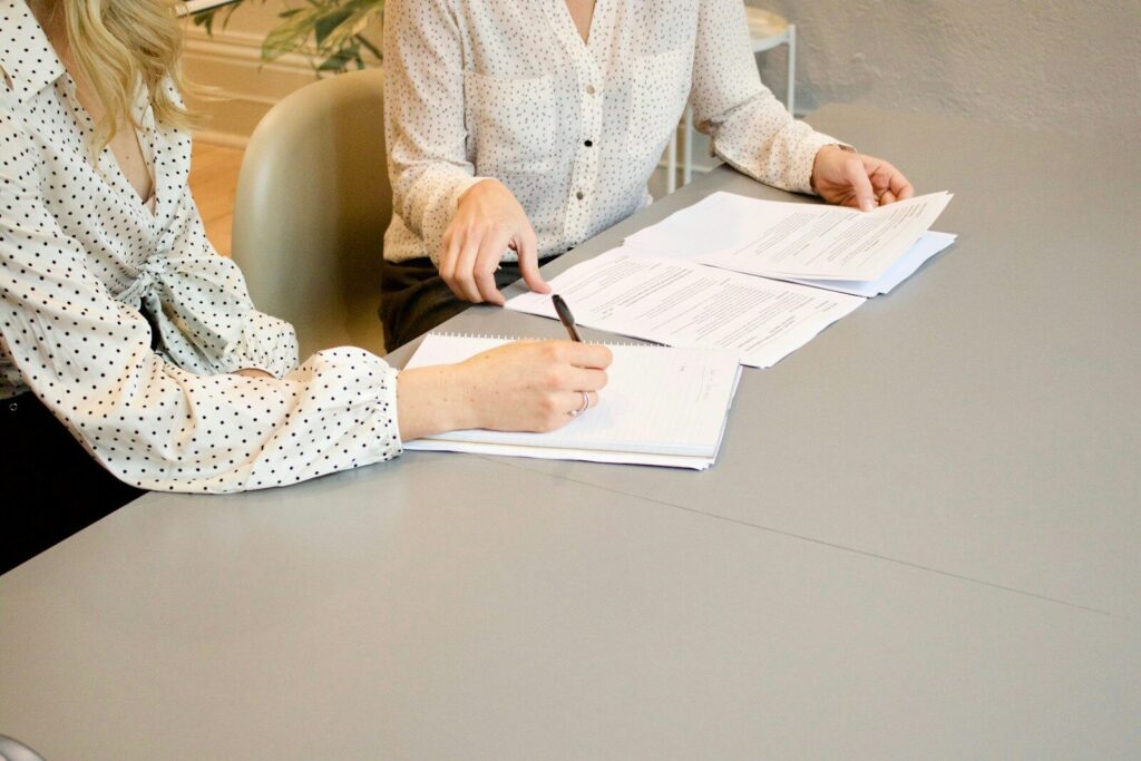 상담을 통해 외도 발견 가능성 경로를 설명해드립니다. woman signing on white printer paper beside woman about to touch the documents